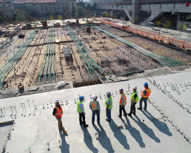 Reihe von Bauarbeitern schreitet über eine großflächige Baustelle