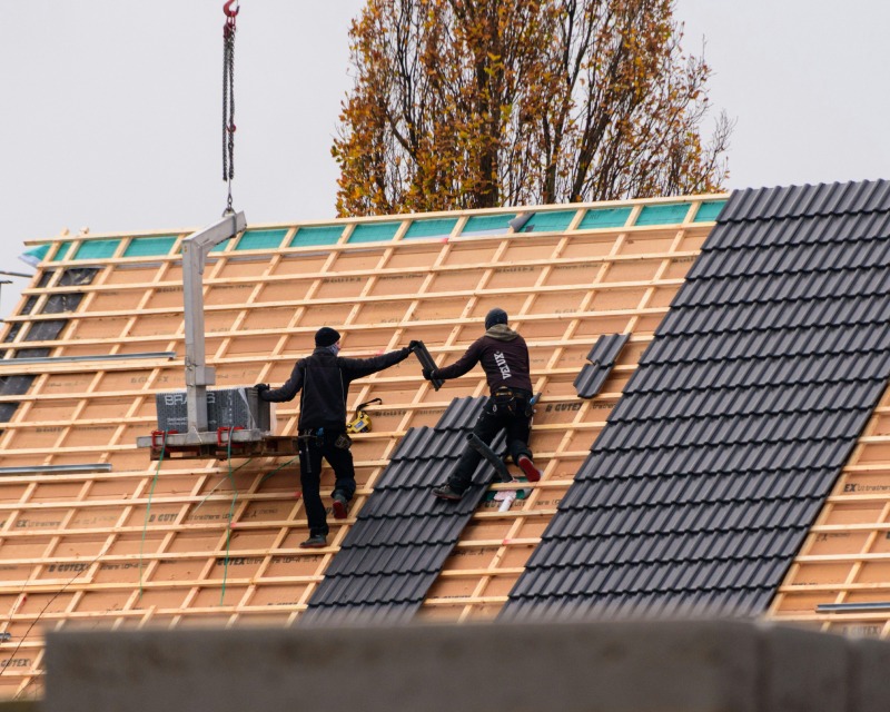 Zwei Dachdecker verlegen Solarmodule auf einem Ziegeldach