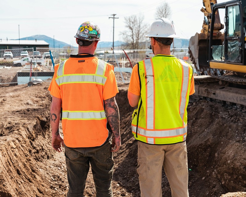Zwei Bauarbeiter in Warnwesten auf einer Baustelle mit Bagger